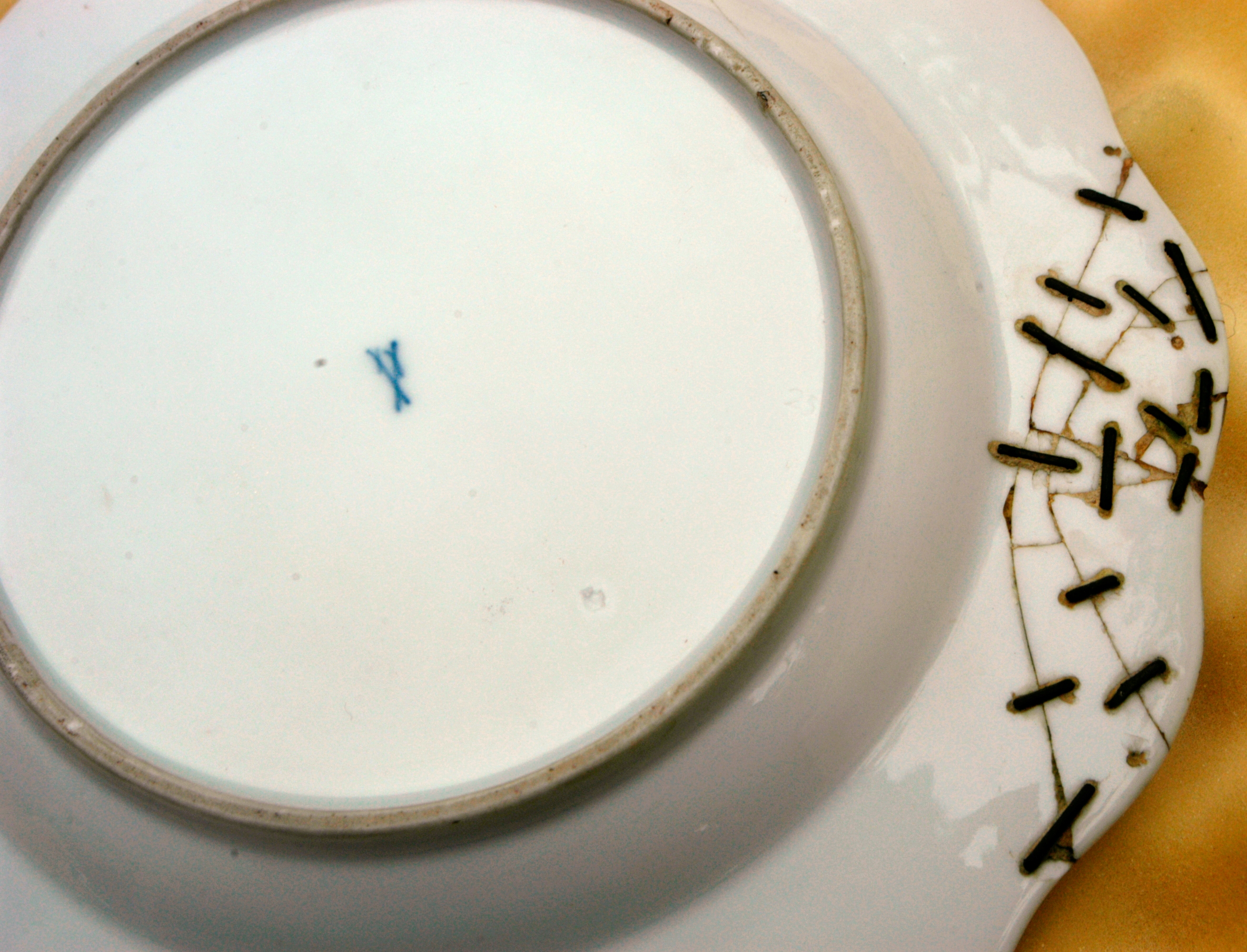 The bottom right side of the ceramic plate has several dark metal staples crossing the seam, and a blue mark is visible on the left side.