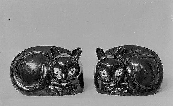 A black and white glazed porcelain cat in a reclining pose, with dark details at the eye positions.